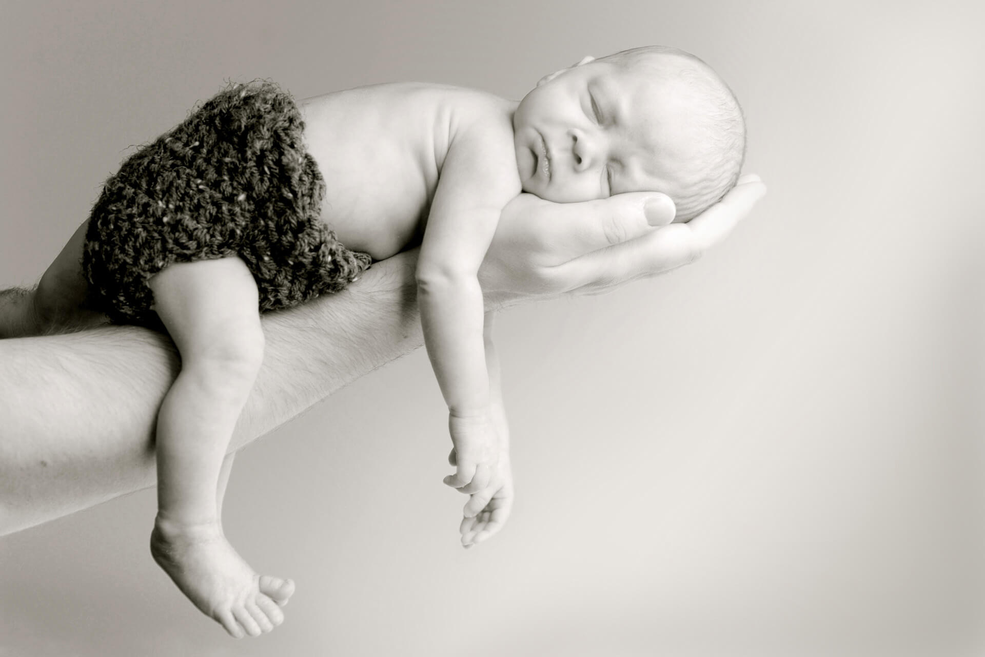 Best Detroit baby photographer's fun and candid newborn photos of a baby zonked in his father's arm in Troy, Michigan.