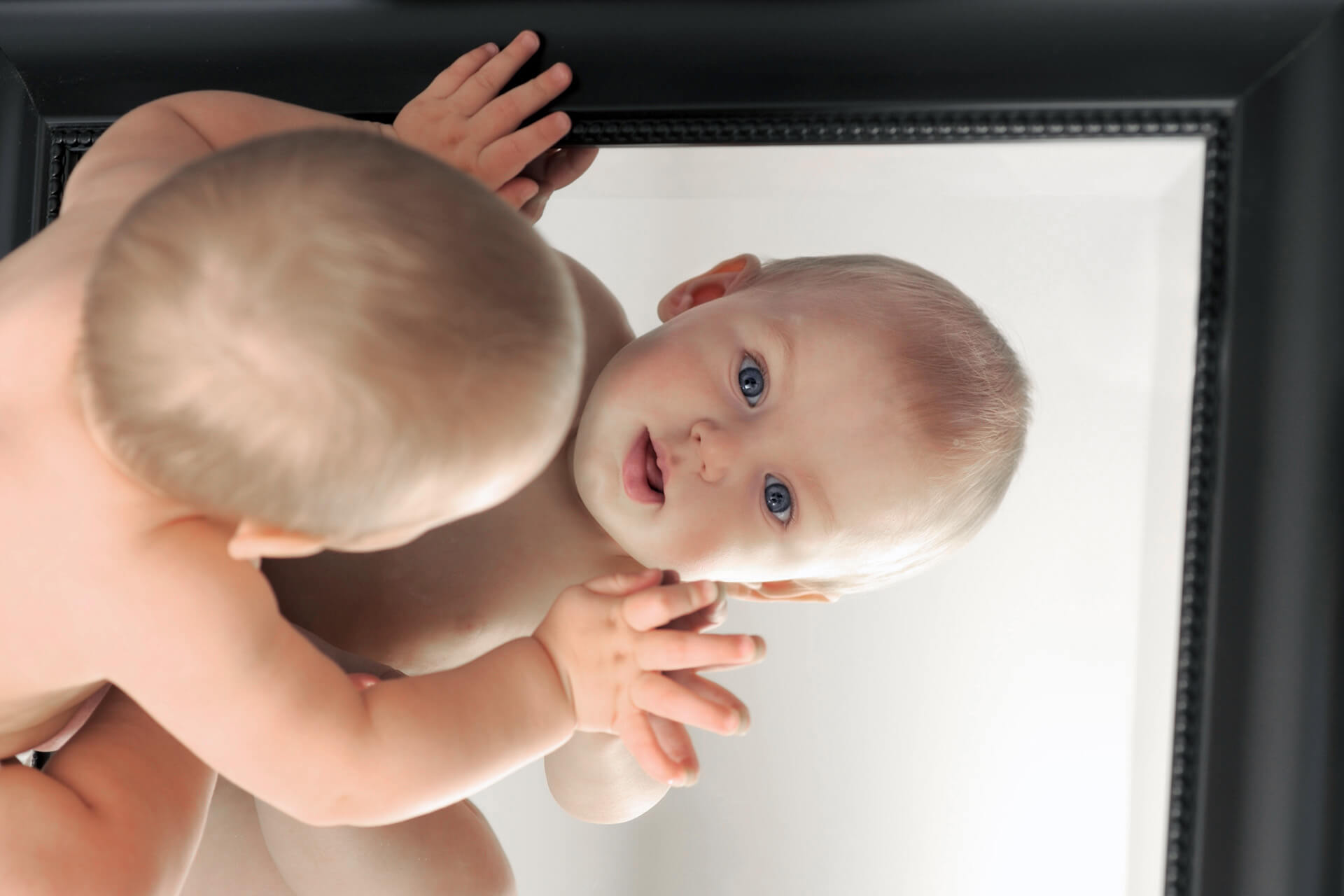 Best Detroit infant photographer's fun and candid baby photos capture newborn fun while a baby checks himself out in a mirror in Detroit, Michigan.