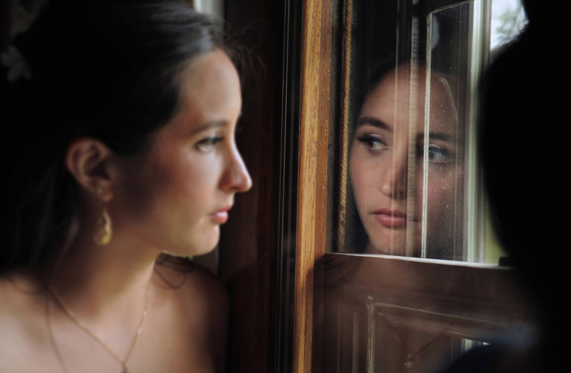 Michigan wedding photographer takes candid photos of a bride nervously looking out a window watching guests arrive for her Addison Oaks wedding in Romeo, Michigan.